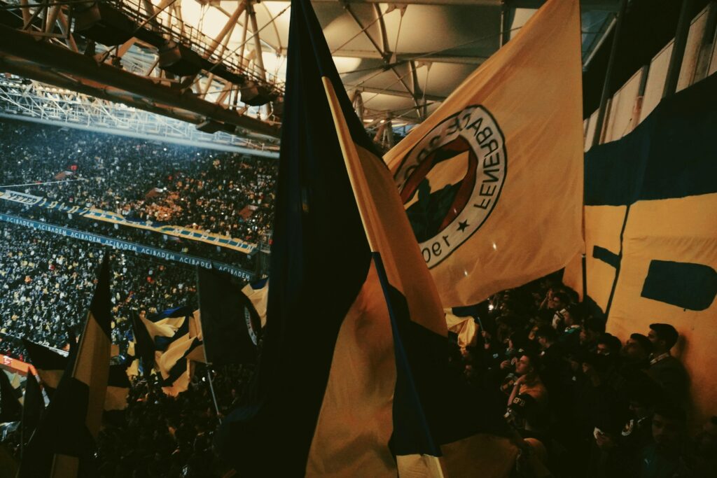 Crowded soccer stadium with fans waving large flags under warm lights.