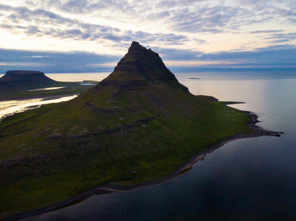A stunning aerial view of Kirkjufell Mountain at sunset in Iceland, mirrored by the surrounding waters.