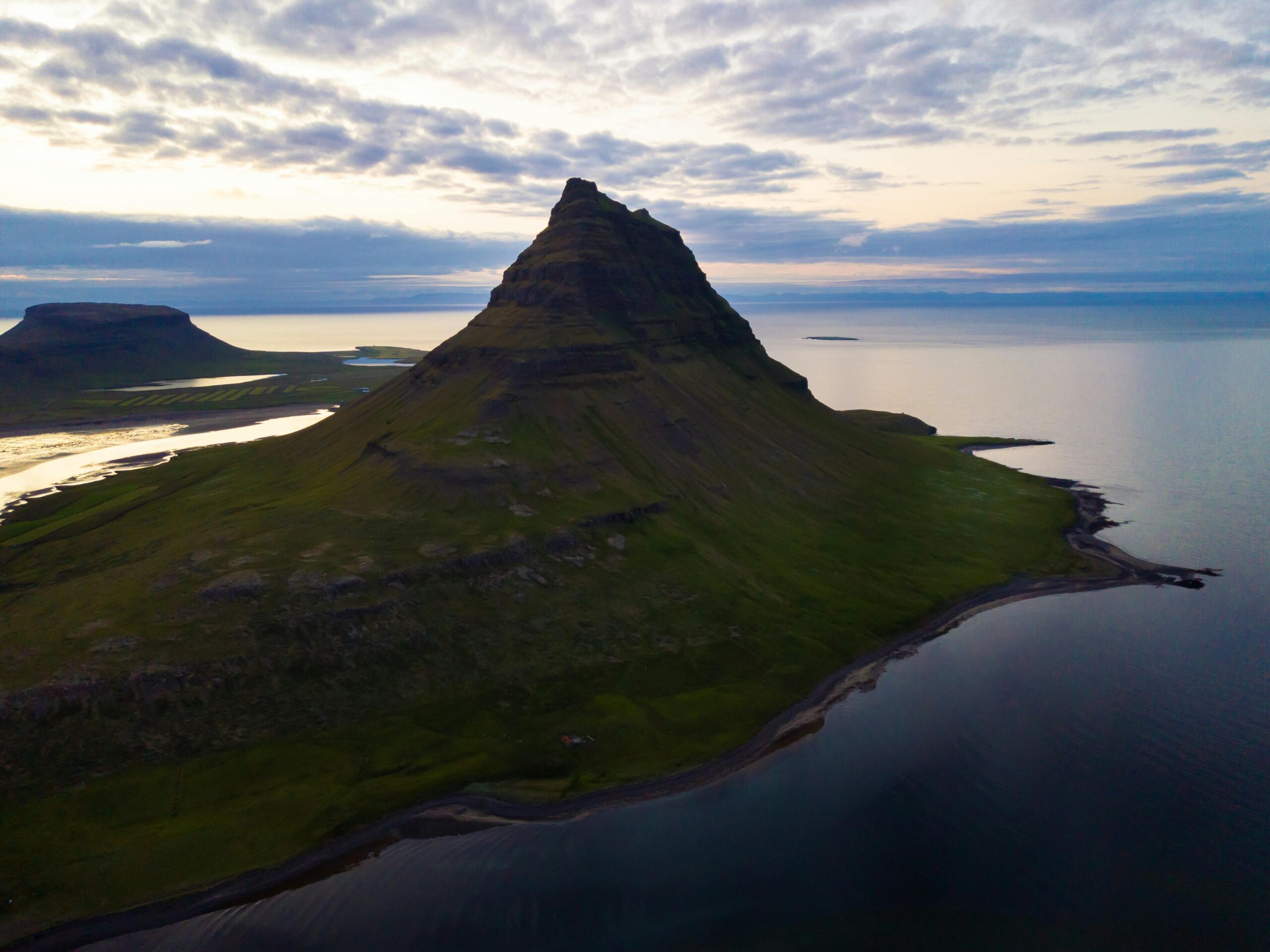 A stunning aerial view of Kirkjufell Mountain at sunset in Iceland, mirrored by the surrounding waters.